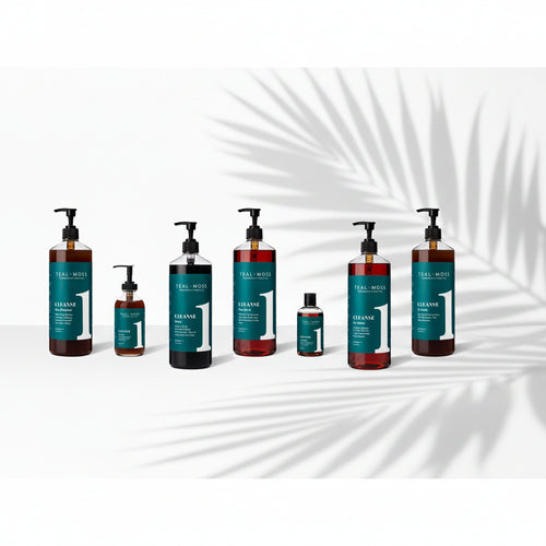 Six bottles of Teal and Moss Cleanser hair care products in various sizes, arranged in a row on a white background. The bottles are amber brown with dark teal labels and black pump dispensers.