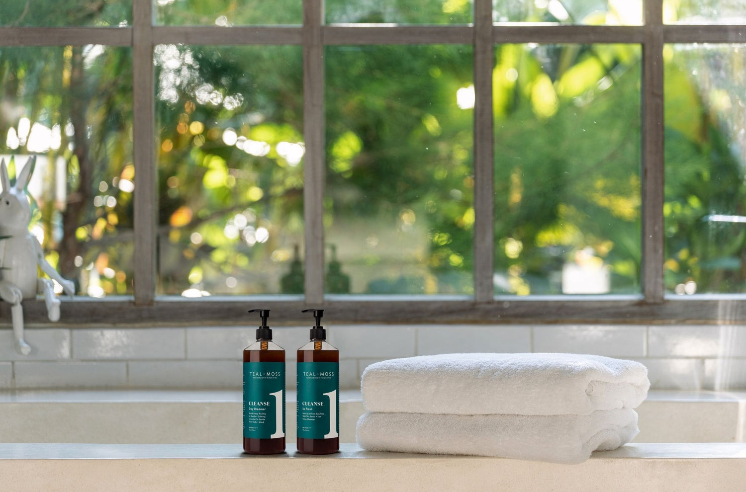 32oz bottles of liquid soap made by Teal and Moss  on a tub near a window with towels